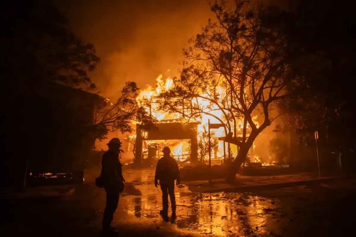 Firefighters watch the flames from the Palisades Fire burning a home during a powerful windstorm on January 8, 2025 in the Pacific Palisades neighborhood of Los Angeles.